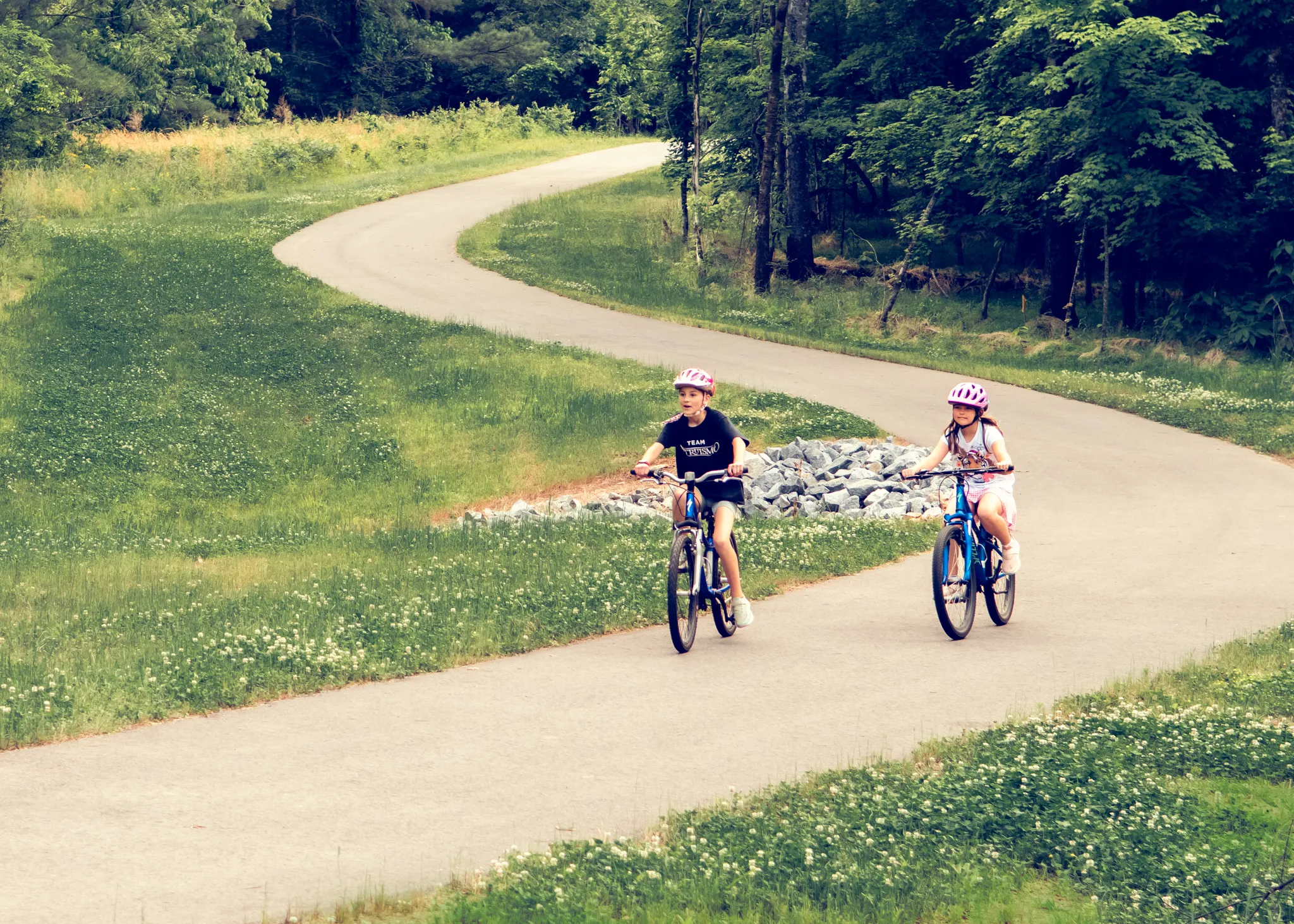 Two children bicycling through an s-curve on the Back Creek Greenway